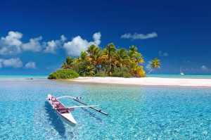 Small outrigger boat off a tiny sandy island in French Polynesia in incredible clear blue sea