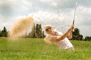 woman playing golf, hitting out of the sand